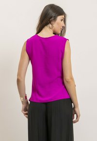 Haut sans manches fuchsia en tissu léger, avec un décolleté en forme de scoop et un ourlet légèrement arrondi. Associé à un pantalon noir fluide.