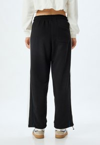 Zwarte, losvallende sweatpants met een elastische tailleband, zijzakken en contrasterende blauwe stiksels langs de buitennaden.
