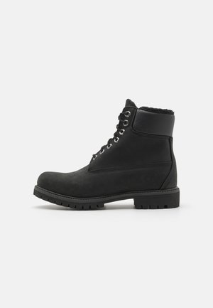 Bottines noires en daim avec une semelle en caoutchouc, dotées d'œillets en métal, de lacets et d'un col en fausse fourrure douce autour du haut.