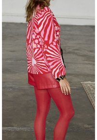 Suéter de punto con patrones en espiral rosa y rojo, detalles en negro, largo por encima de la cadera, combinado con pantalones cortos de cuero sintético rojo y medias.