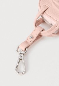 Roh svetloružovej koženej tašky so strieborným kovovým zapínaním a viditeľným zipsom na bielom pozadí.