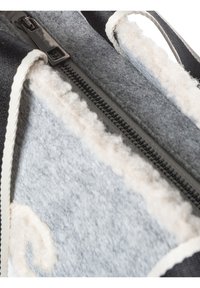 Grijze vilten tas met witte, pluizige rand, voorzien van een zwarte ritssluiting en gebroken-witte accenten. Het ontwerp bevat strakke lijnen en gestructureerde oppervlakken.