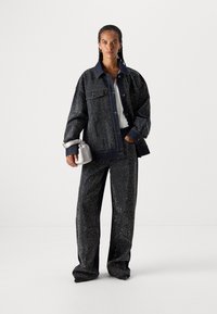 Chaqueta de mezclilla azul marino y pantalones a juego con un patrón de manchas blancas, con ajuste extragrande, gran cuello y dos bolsillos frontales, combinados con un pequeño bolso gris.