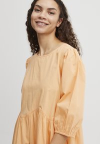 Perzikgekleurde katoenen jurk met een ronde halslijn, driekwart pofmouwen en een geraffineerde taille, met een relaxte pasvorm.