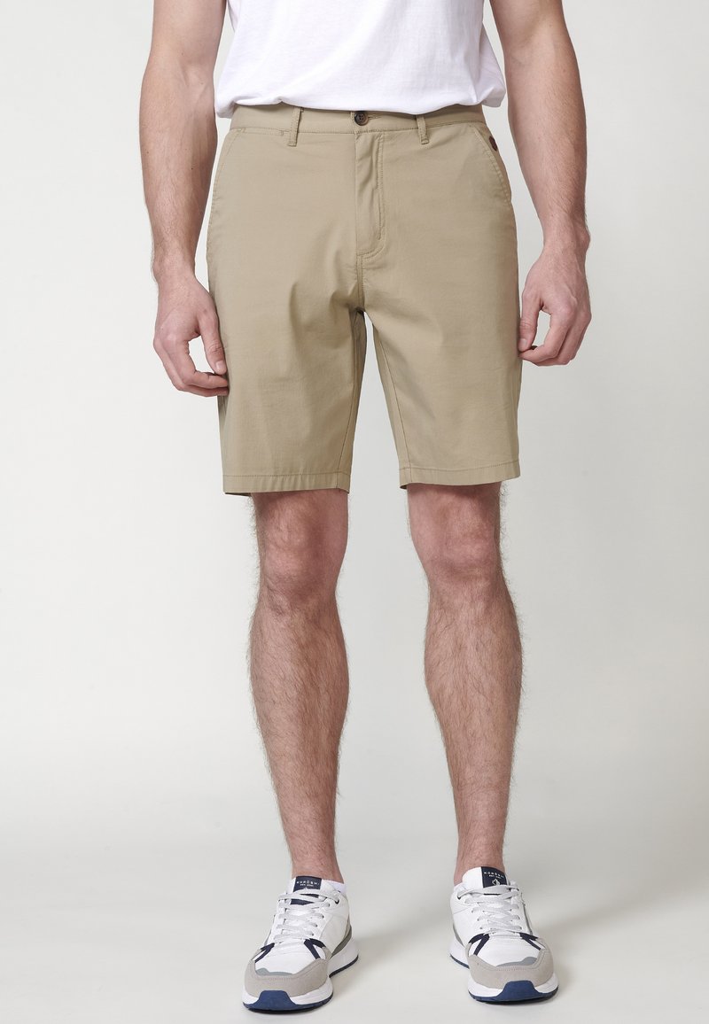 Pantaloni scurți khaki cu închidere cu nasture, buzunare laterale și o textură fină. Purtați cu un tricou alb și pantofi sport albi.