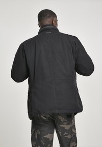 Zwarte buitenjas met kraag, met een ontspannen pasvorm, textuurstof en zijzakken. Camo-gepatenteerde broek maakt de look compleet.