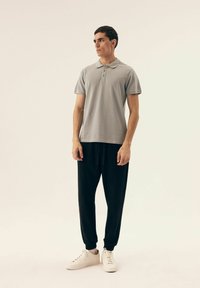 Szary polo z kołnierzykiem i trzema guzikami, w połączeniu z czarnymi dresami i białymi sneakersami, stojący na neutralnym tle.