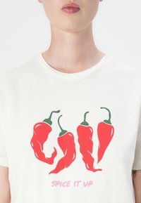 White cotton t-shirt featuring four stylized red chili peppers with green stems, text "SPICE IT UP" in pink below the graphic design.