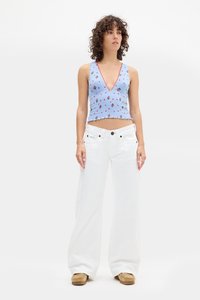 Top corto azul con flores y un profundo escote en V, combinado con pantalones vaqueros anchos blancos. La tela parece suave con un diseño texturizado.