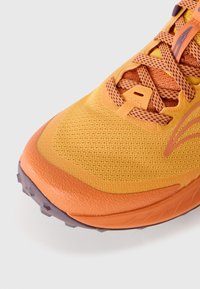 Baskets de sport orange et jaunes avec tige en mesh, semelle en caoutchouc texturée et accents violets contrastants sur les orteils et les lacets.