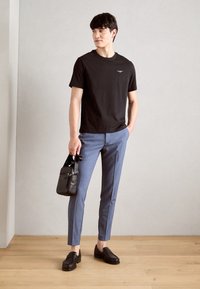 Zwarte katoenen t-shirt, lichtblauwe op maat gemaakte broek, zwarte leren loafers en een kleine crossbody tas met een ritsdetail.