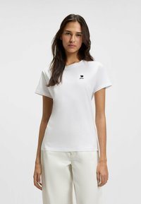 White cotton t-shirt with short sleeves, round neck, featuring a small black heart logo and text on the left chest area.