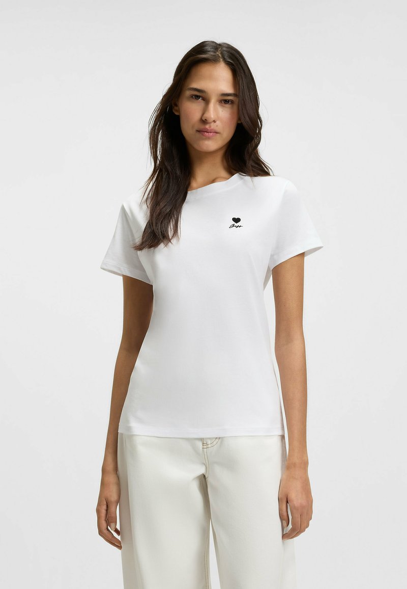 White cotton t-shirt with short sleeves, round neck, featuring a small black heart logo and text on the left chest area.