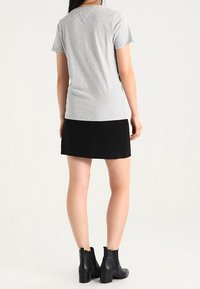 Camiseta gris de manga corta combinada con una falda negra, llevada con botines negros hasta el tobillo. La camiseta presenta un diseño y textura sencillos.