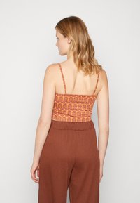 Top court à motifs orange avec des fines bretelles, associé à un pantalon large marron, doté d'un tissu texturé et d'une taille élastique.