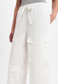 Witte cargobroek met een elastische tailleband en trekkoord. Heeft meerdere voorzakken en een losse, wijde pasvorm. Heeft een soepele textuur.