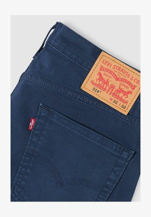 Pantalones de mezclilla azul con un parche trasero de cuero marrón etiquetado "Levi Strauss & Co.", con costuras rojas y una pequeña etiqueta roja en el bolsillo.