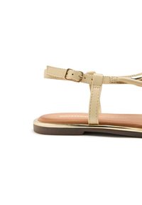 Sandalia beige de tiras con suela plana, con una textura suave, una hebilla dorada y una plantilla marrón. Diseño minimalista con tiras delgadas.