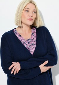 Marinblå stickad tröja med V-hals över en rosa blommig topp. Mjuk textur och avslappnad passform, med långa ärmar och ribbade ärmslut.