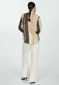 Camicia a maniche lunghe a motivo con righe verticali in tonalità terrose, abbinata a pantaloni a gamba larga color crema e sandali con tacco.