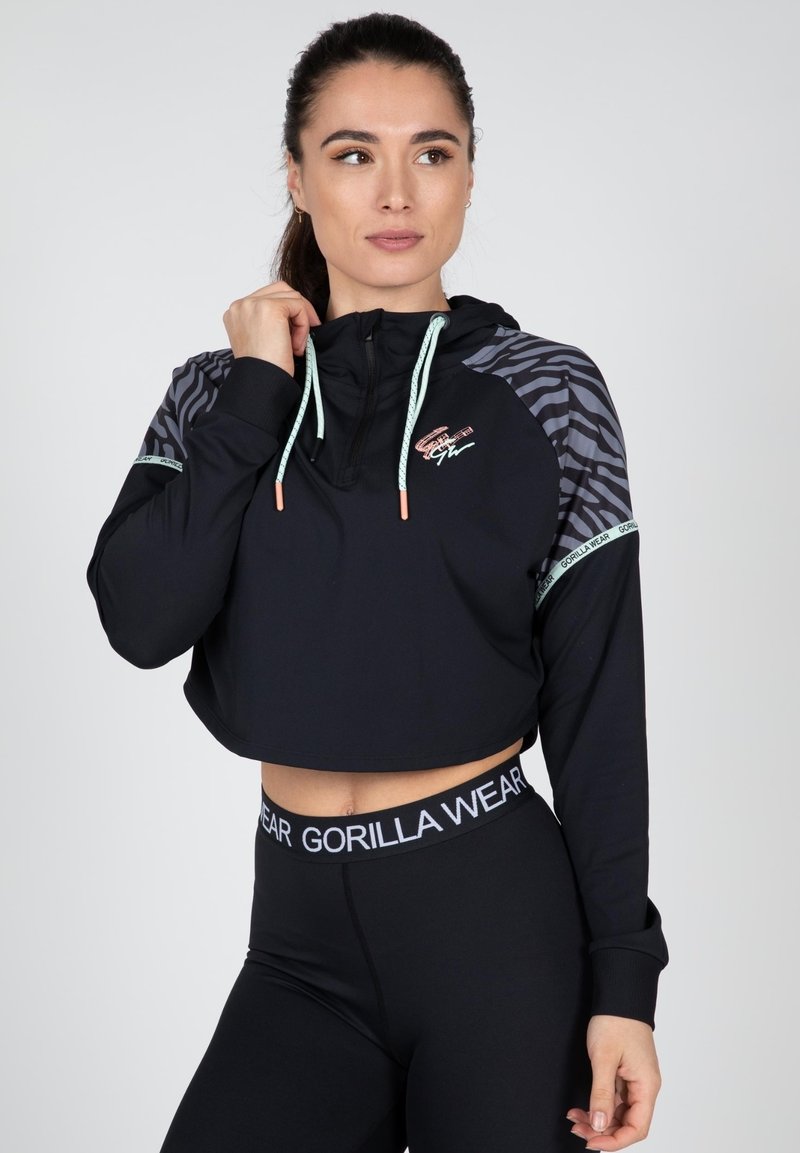 Zwarte cropped hoodie met een ritssluiting bij de kraag, gestreepte zwart-grijze patronen op de mouwen, aqua trekkoorden en logodetails. Gecoördineerd met zwarte leggings.