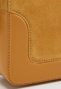 Torebka skórzana w kolorze tan, z gładkim wykończeniem oraz kontrastującą panelą z zamszu, o prostych liniach i starannym szwie wzdłuż krawędzi.