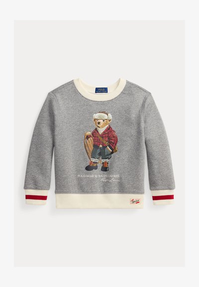 Sudadera gris con un oso vestido con una camisa de cuadros roja, sosteniendo un trineo. Puños acanalados en crema con acentos rojos, etiqueta del logo en el dobladillo.