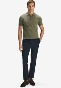 Oliivinvihreä polo-paita, jossa on teksturoitu kangas, lyhyet hihat ja kolmesta napista koostuva kaitale; yhdistettynä tummansinisiin housuihin ja ruskeisiin kenkiin.