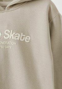 Beige hoodie with a textured fabric, featuring a front print that reads "Skate Generation" in bold cream letters. Casual design with a hood.
