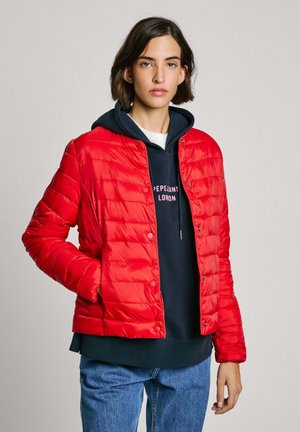 Rode gewatteerde pufferjack met een drukknopen sluiting aan de voorkant. Gekleed over een marineblauwe hoodie. Heeft een gladde textuur en een cropped ontwerp.