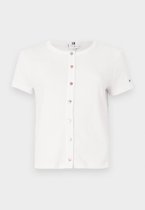T-shirt blanc à manches courtes en coton avec un col rond, doté de boutons couleur or rose sur le devant et d'un petit logo sur la manche.