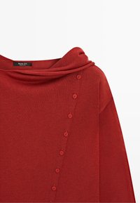 Red knit sweater with diagonal button detail and a wide, folded neckline on a plain background.