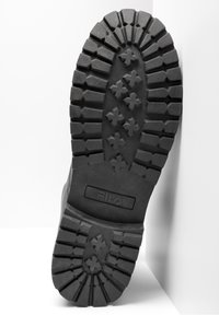 Svart gummisåle til sneakers med dype såler med stjernesymmetriske mønstre, teksturert overflate, og Fila-logoen preget nær hælen.