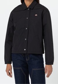 Chaqueta negra de botón, hecha de un tejido suave, con un cuello clásico, dos bolsillos laterales y un logo en el lado izquierdo del pecho.