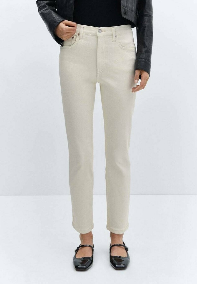 Jeans de color beige claro, hechos de algodón, con cinco bolsillos, cierre de botón y un diseño ajustado. Llevados con zapatos planos negros.