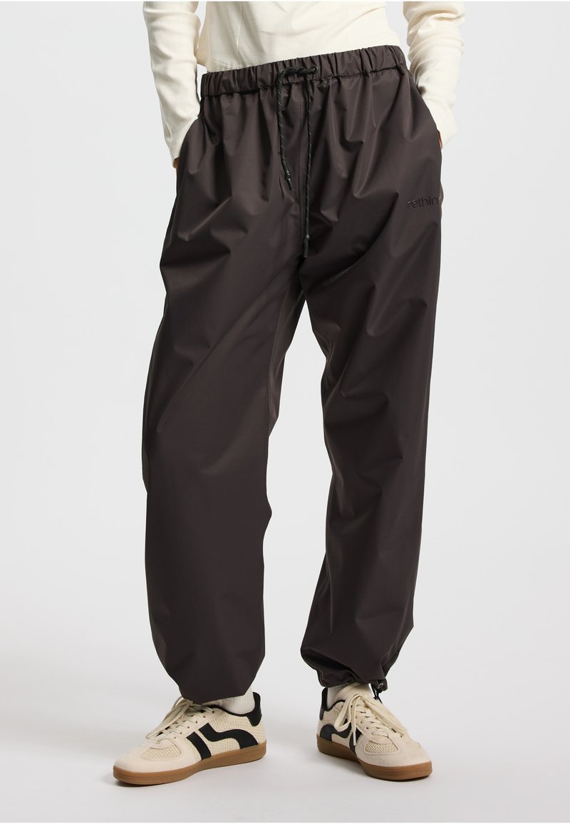 Pantaloni neri resistenti all'acqua con vita elasticizzata e coulisse regolabile. Vestibilità ampia, tessuto liscio e tasche laterali con cerniera.