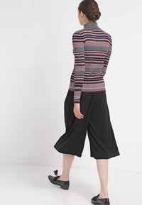 Tajta, ribbade turtlenecks med svarta, röda och grå ränder. Kombinerat med lösa, korta svarta byxor. Svarta skor med dekorativa detaljer.