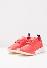 Červené síťované tenisky s třemi bočními pruhy, polstrovaným jazykem a bílou mezipodešví. Mají texturovaný svršek a gumovou podrážku pro lepší přilnavost.