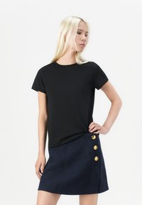 Black short-sleeve t-shirt with a round neck and subtle logo; paired with a navy textured skirt featuring three gold buttons on the side.