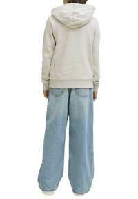 Sweatshirt gris à capuche et jean large bleu clair. Le sweatshirt a une poche kangourou et des poignets côtelés, tandis que le jean présente des poches arrière.