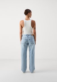 Άσπρο ριγέ μπλουζάκι χωρίς μανίκια συνδυασμένο με ανοιχτά μπλε φαρδιά τζιν παντελόνια. Τα τζιν διαθέτουν κλασικό σχέδιο πέντε τσεπών και δερμάτινη ταμπέλα στο πίσω μέρος.