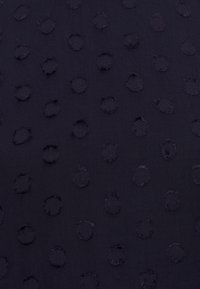 Marinfärgad tyg med en texturerad yta som har upphöjda cirkulära mönster, jämnt fördelade över materialet. Mjuk textur, lättvikts.