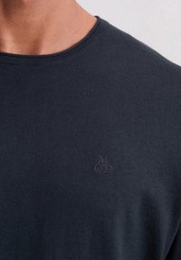Dunkelblaues T-Shirt mit kurzen Ärmeln aus weichem Stoff, mit einem dezent geprägten Logo auf der linken Brustseite und einem klassischen Rundhalsausschnitt.