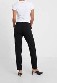 Zwarte op maat gemaakte broek met een slim fit en details van achterzakken, gecombineerd met een aansluitend wit t-shirt, aangevuld met zwarte hoge muiltjes.