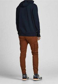 Felpa con cappuccio blu navy, pantaloni cargo marroni con tasche laterali e scarpe da ginnastica grigie con dettagli arancioni. Vista posteriore, vestibilità casual, tessuto morbido.