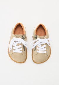 Beige mockasinsneakers med vita snören och en texturerad gummisula. Har siddragkedja och mjukt innerfoder i ljusbrunt.