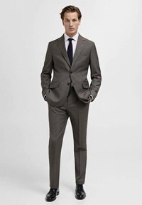 Gray suit with a tailored fit, featuring a notch lapel, two buttons, and side pockets. Paired with a white shirt and a dark tie. Black shoes.
