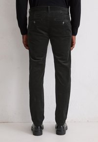 Pantalon en velours côtelé noir avec une coupe slim, doté de deux poches arrière et de passants de ceinture, associé à des chaussures en cuir noir. Texture lisse et couleur uniforme.