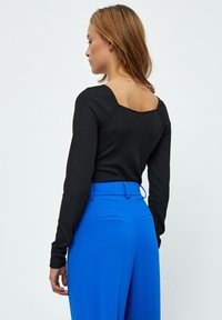 Zwarte geribbelde lange mouw top met een vierkante halslijn, gecombineerd met felblauwe high-waisted broek met zijzakken.
