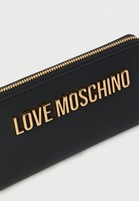 Μαύρο πορτοφόλι από συνθετικό δέρμα με χρυσά γράμματα "LOVE MOSCHINO", χρυστό φερμουάρ και λεία υφή. Μινιμαλιστικός σχεδιασμός.